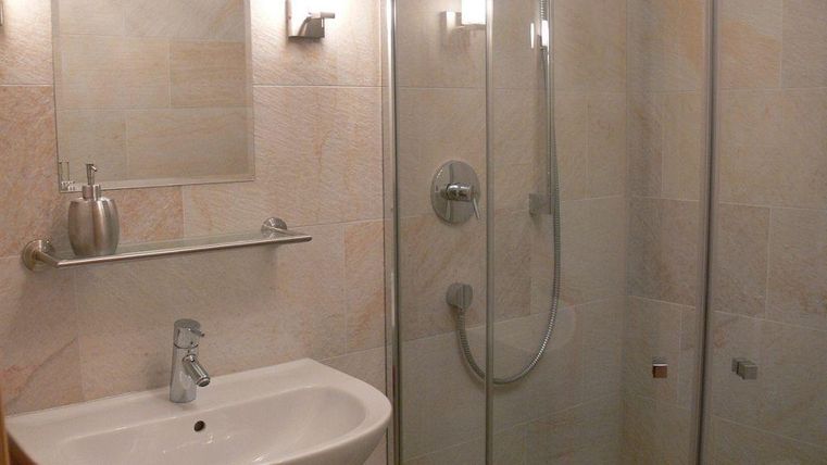 Een moderne badkamer met een douche en een wastafel. De muren zijn licht met licht gestructureerde tegels.