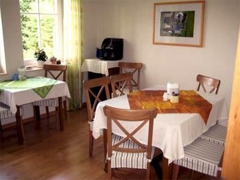 Une salle à manger confortable avec plusieurs tables et chaises. Les fenêtres laissent entrer beaucoup de lumière et de petites décorations donnent à la pièce une atmosphère accueillante.
