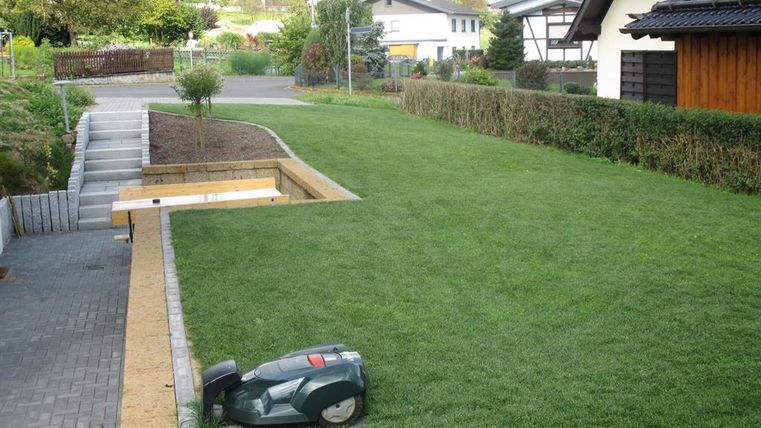 Un jardin bien entretenu avec une pelouse verte et un chemin en pierres. Au premier plan se trouve une tondeuse à gazon.