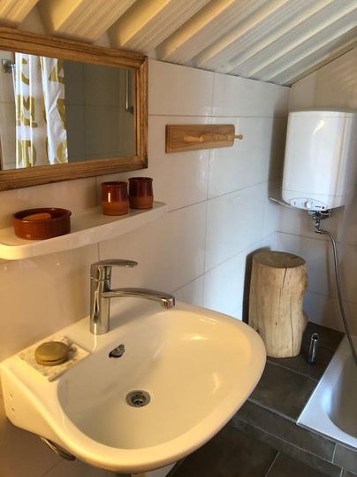 A modern bathroom with a sink, a mirror, and a wooden bench. The walls are brightly tiled, and there are some decorative items.