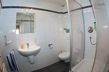 Une salle de bain moderne avec des carreaux blancs et une douche. Il y a un lavabo, des toilettes et un grand miroir.