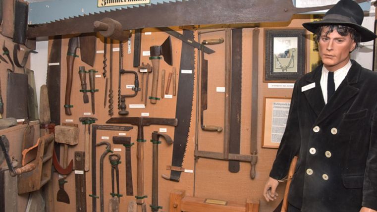 Ein Zimmermanns-Museum mit verschiedenen Werkzeugen an der Wand. Neben den Werkzeugen steht eine lebensgroße Figur eines Zimmermanns.