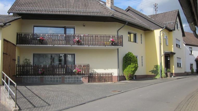 Een modern huis met twee balkons en bloeiende planten. De gevel is in lichte kleuren en de omgeving is goed onderhouden.