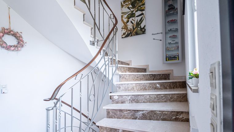 Een elegante trap met gemarmerde treden en een handgemaakt leuning. Aan de muur hangt een modern kunstwerk en de entree straalt een uitnodigende sfeer uit.