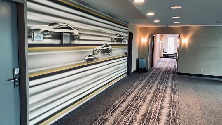 A modern hallway with a mural of cars. The floor is designed with a carpet featuring tire track patterns.