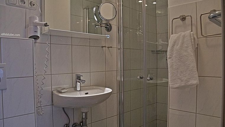 Une salle de bain moderne avec une douche et un petit lavabo. Des carreaux blancs et un porte-serviette sont également visibles.