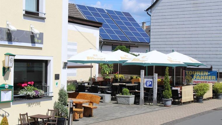A cozy café with umbrellas and outdoor seating on a quiet street. Solar panels can be seen on the roof in the background.