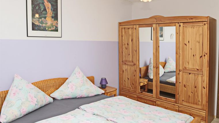 Een gezellig slaapkamer met een tweepersoonsbed en kleurrijke kussens. Een grote houten kast en een kunstwerk aan de muur aanvullen de inrichting.