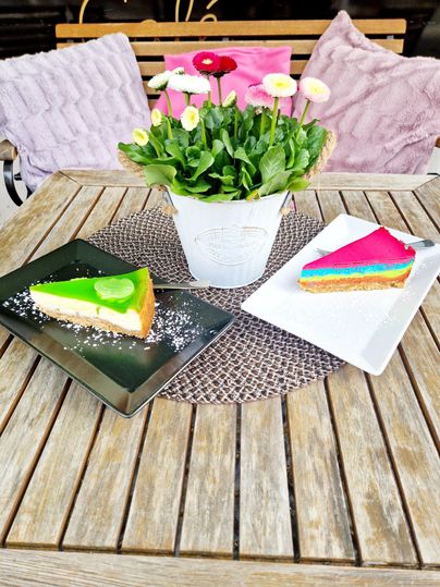 Deux morceaux de gâteau colorés sur une table en bois, entourés d'une plante en fleurs dans un pot blanc. La table a un élégant set de table et est décorée de manière conviviale.