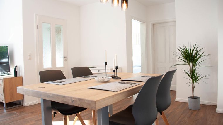 Ein moderner Essbereich mit einem Holztablett und schwarzen Stühlen. Eine grüne Pflanze steht in der Ecke und der Raum hat viel natürliches Licht.