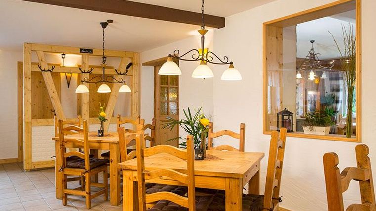 A cozy dining hall with wooden chairs and tables. The walls are bright, and plants create an inviting atmosphere.