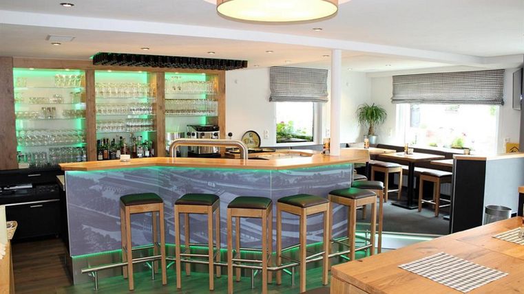 Eine moderne Bar mit Holzstühlen und einer stilvollen Theke. Sanftes Licht und Pflanzen schaffen eine einladende Atmosphäre.