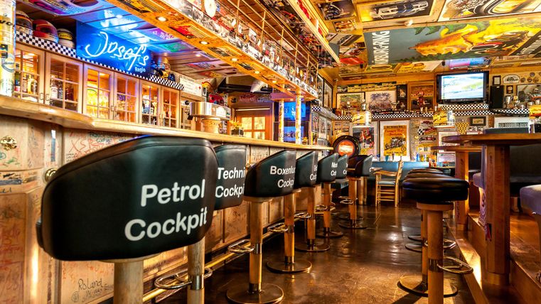 A stylish bar with unique cockpit chairs and colorful wall decorations. The atmosphere is lively and inviting.