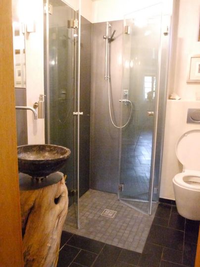A modern bathroom with a glass shower and an elegant wooden wash basin. The toilet is designed in a minimalist style.