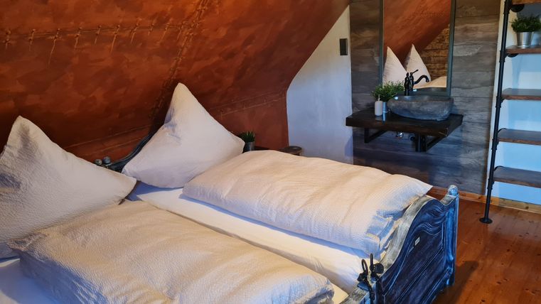 Een gezellige slaapkamer met twee bedden en een houten vloer. Aan de muur hangt een spiegel, en een trap leidt naar boven.