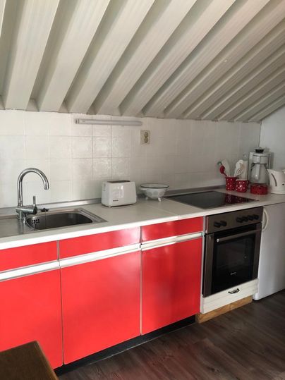 A modern kitchenette with red cabinets and white tiles. The space is well-organized and has basic kitchen appliances like a toaster and a coffee maker.