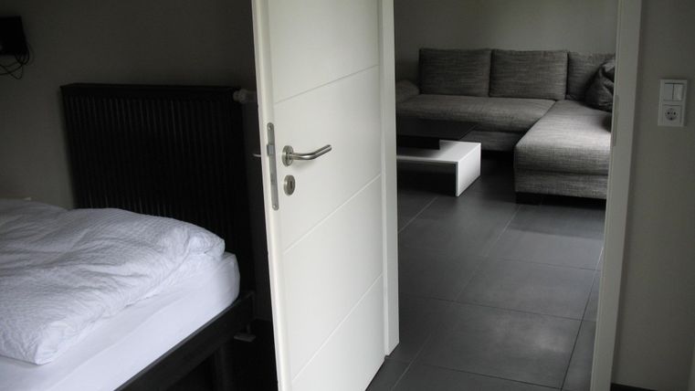 Ein moderner Raum mit einem Schlafzimmer und einem Wohnbereich. Die Möbel sind schlicht und stilvoll, mit einem grauen Sofa und einem kleinen Tisch.