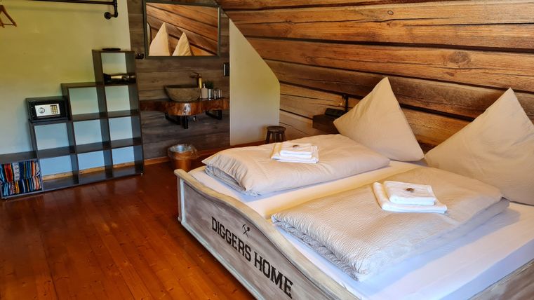 Een gezellige slaapkamer met twee bedden, kussens en frisse handdoeken. De muren zijn van hout, en een plank staat in de kamer.