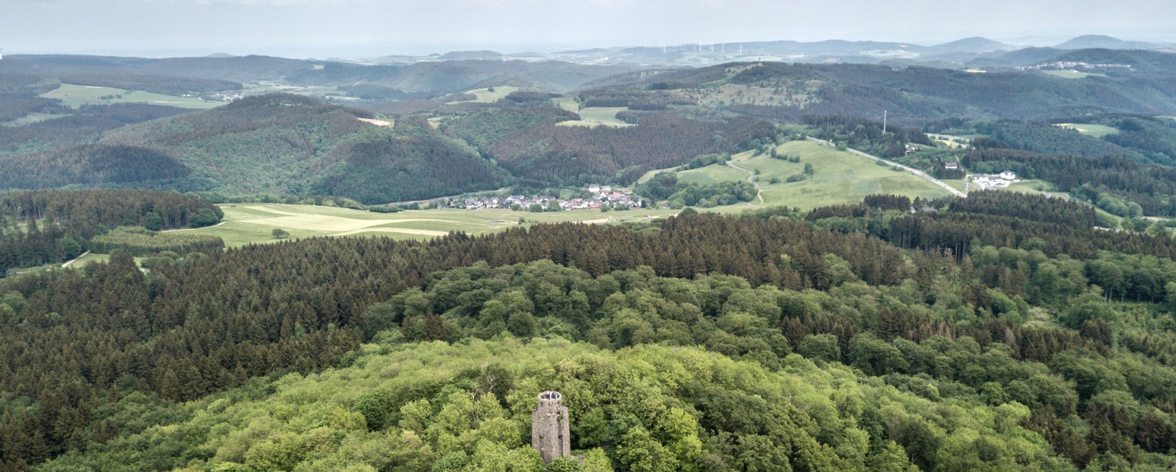 Luftaufnahme der Hohen Acht mit Aussichtsturm, umgeben von dichtem Wald und Hügeln unter bewölktem Himmel., © Eifel Tourismus GmbH, Domink Ketz