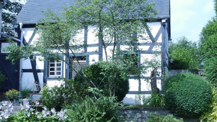 A traditional half-timbered house with a beautiful garden. Trees and flowers surround the building, creating an inviting atmosphere.