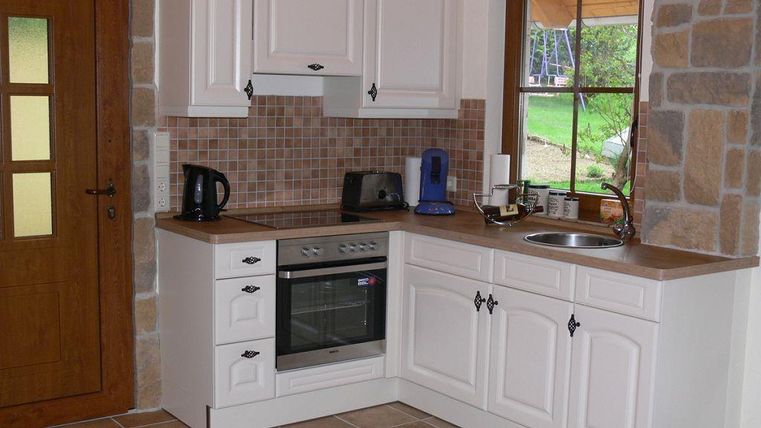 Een moderne keuken met witte kasten en een heldere houten werkblad. De uitrusting omvat een fornuis, een waterkoker en een gootsteen.