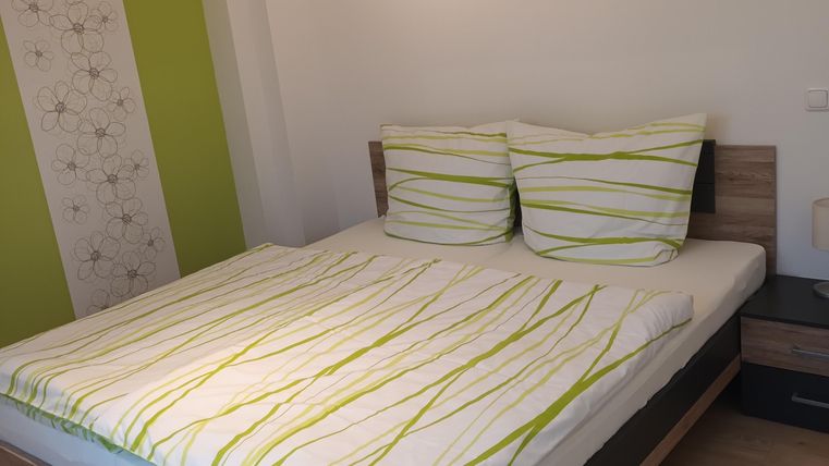 Een moderne slaapkamer met een tweepersoonsbed en gestreepte dekens. De muren zijn licht geverfd en er staat een nachtkastje naast het bed.