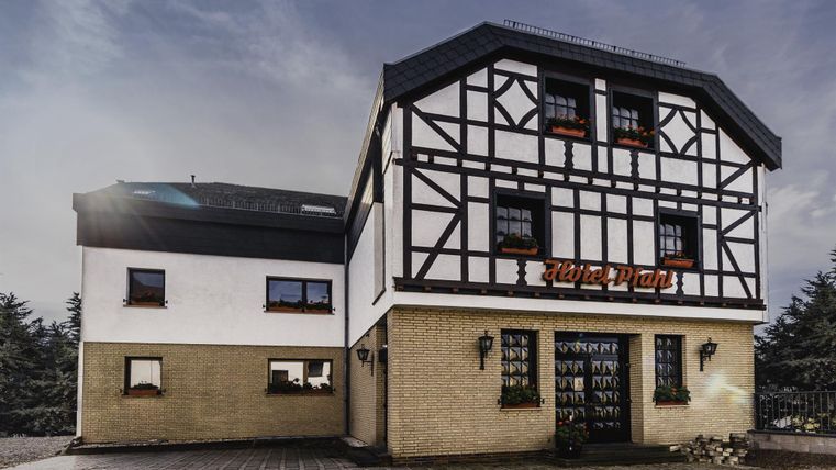 Een traditioneel vakwerkhuis met een moderne uitbouw. De gevel is licht en vriendelijk, omringd door een geplaveide ruimte.