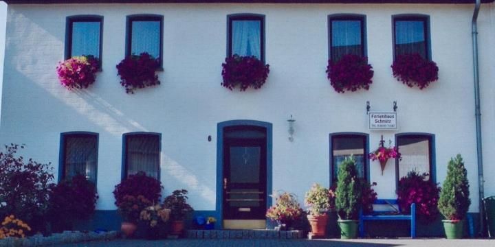 A charming house with flower baskets at the windows. Colorful plants and inviting seating adorn the entrance area.