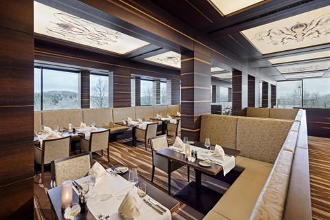 An elegant restaurant with stylish tables and comfortable benches. Generous windows provide a view of the surroundings.