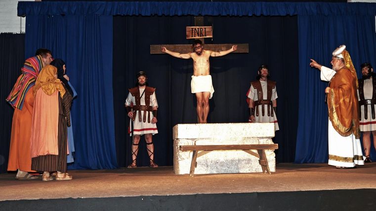 Eine Theateraufführung mit Schauspielern in historischen Gewändern. Im Mittelpunkt steht eine figurative Darstellung der Kreuzigung.