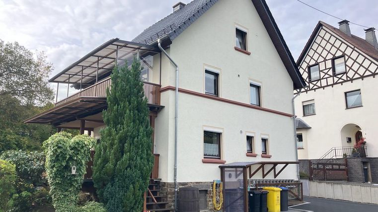 Une maison moderne avec un balcon et un environnement bien entretenu.
Au premier plan, il y a des poubelles colorées et un jardin bien conçu.