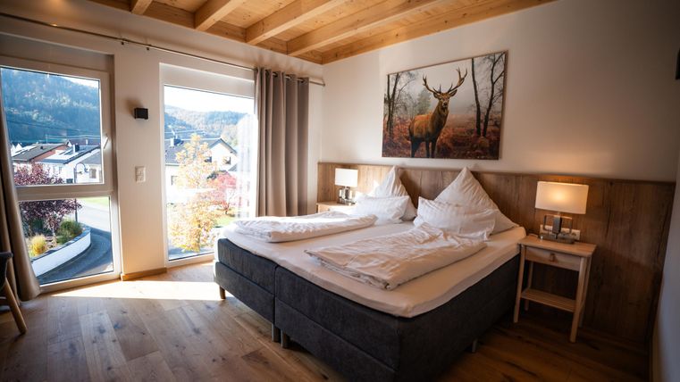 Een moderne slaapkamer met een tweepersoonsbed en een houten plafond. Grote ramen bieden uitzicht op het landschap.