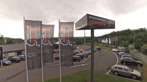 Ein Autohaus mit mehreren Verkaufsflaggen und einer großen Anzeige. Auf dem Parkplatz stehen viele Fahrzeuge.