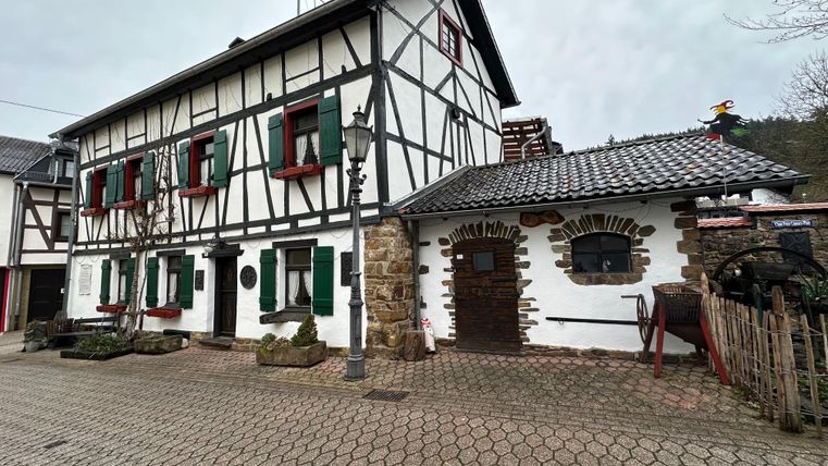 Een charmant vakwerkhuis met groene luiken. De gevel is wit met donkere houten frames en heeft een aangrenzend geplaveid plein.