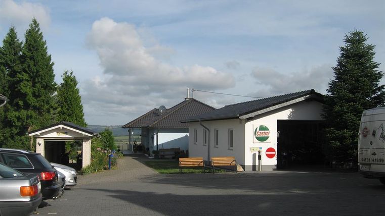 A quiet courtyard with buildings and a paved driveway. In the background, there are trees and a clear sky.