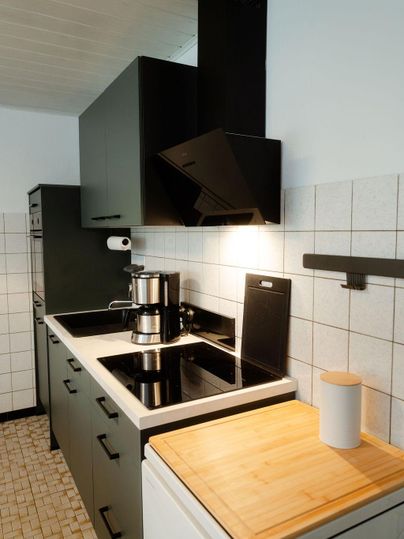 Eine moderne Küche mit schwarzen Hochglanz-Schränken und einem klaren, einfachen Design. Die Kochfläche ist gut ausgestattet und es gibt eine Holzarbeitsplatte.