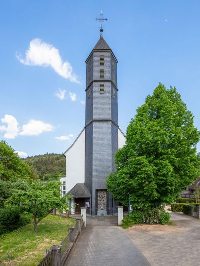 Eine schöne Kirche mit einem hohen Turm und einem Kreuz an der Spitze. Umgeben von üppigem Grün und blauem Himmel.