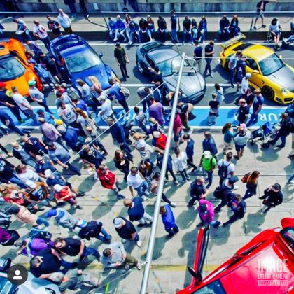 Eine große Menschenmenge steht in einer belebten Straße, umgeben von verschiedenen Autos. Das Bild zeigt eine lebhafte Atmosphäre mit vielen Leuten, die sich versammeln.