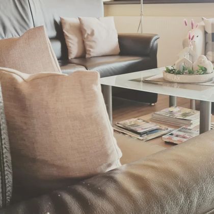 A cozy living room with a brown leather couch and cushions. On the table, there is a decoration with a small Easter bunny and magazines.