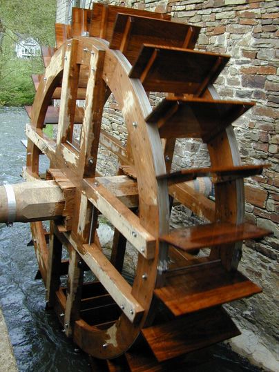 Ein Wasserrad aus Holz, das an einem Fluss installiert ist. Es dreht sich durch die Strömung des Wassers.
