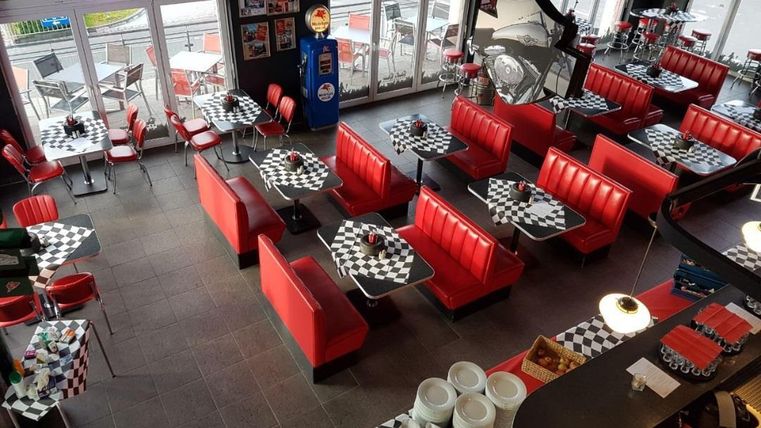 Un restaurant moderne avec des bancs rouges et des tables à carreaux noir et blanc. De grandes fenêtres laissent entrer beaucoup de lumière naturelle et créent une atmosphère accueillante.