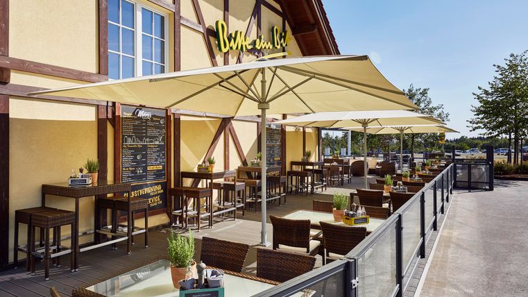 Une terrasse extérieure accueillante d'un restaurant avec des parasols et des places assises confortables. La journée ensoleillée crée une atmosphère détendue.