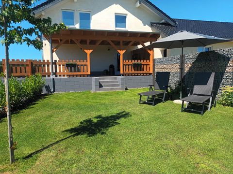 Een mooie tuin met een terras en twee ligstoelen. Op de achtergrond staat een modern huis.