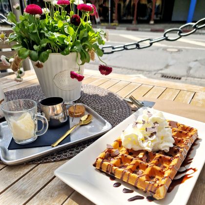 Un plat de gaufres délicieux avec sauce au chocolat et crème chantilly dans une assiette. À côté se trouve un petit bouquet de fleurs et une tasse avec une garniture sucrée.