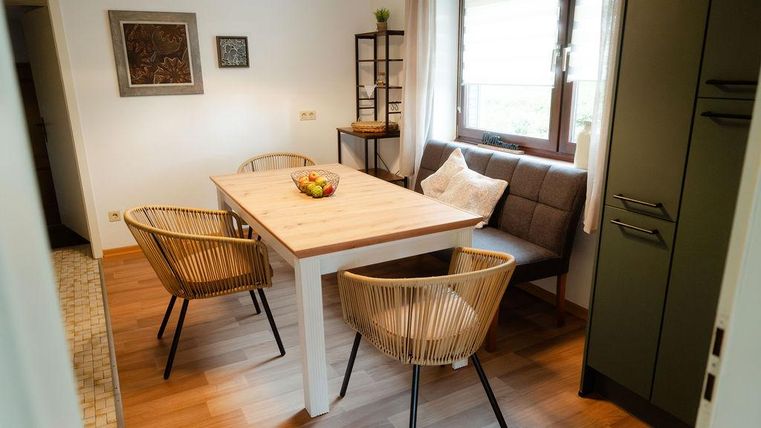 Ein gemütlicher Essbereich mit einem Holztisch und Stühlen. Durch das Fenster fällt natürliches Licht, und frisches Obst steht auf dem Tisch.