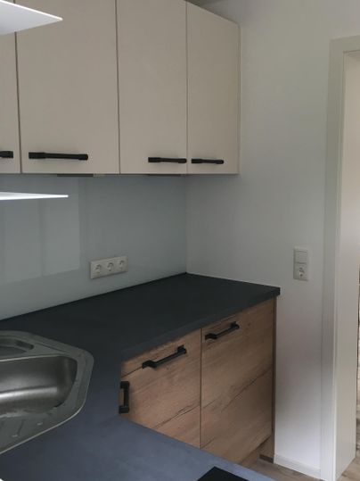 Une cuisine moderne avec des armoires blanches et un panneau en bois. Le plan de travail est sombre et la pièce semble lumineuse et accueillante.