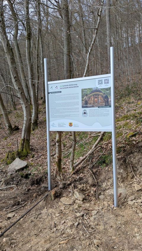 An information sign about the Kolbenbergweg in a forested area. It features an image of the historic Kolben Bridge and includes information about the surroundings.