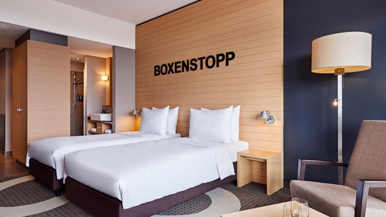 A modern hotel room with two single beds and stylish decor. On the wall is the inscription "BOXENSTOPP".