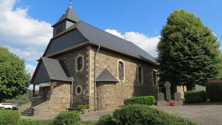 St. Hubertuskapelle in Wimbach, umgeben von Bäumen und Sträuchern, bei sonnigem Wetter.