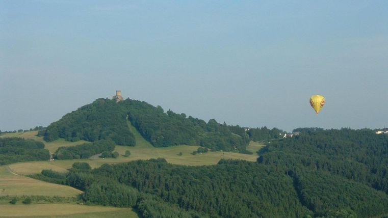 Une colline verte avec une ancienne ruine au sommet. Un montgolfière flotte doucement dans l'air.